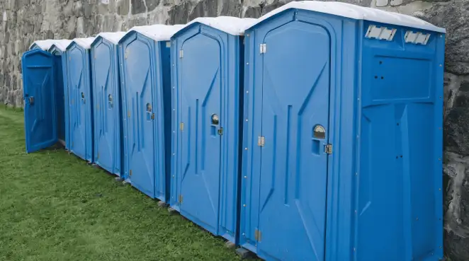 Row of blue portable toilets lined up on grass against a stone wall for event sanitation in Stockton, CA