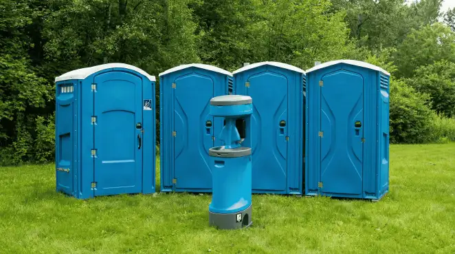 Four blue portable toilets and a matching hand washing station on grass near trees, a common sight at local outdoor events in Stockton, CA