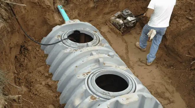 Septic tank installation showing a technician compacting soil around a new poly septic tank in an excavation pit in Stockton, CA